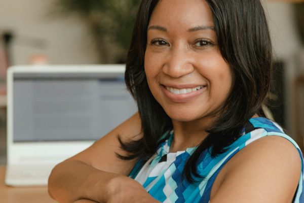 Woman sitting at a desk smiling with a Macbook behind her